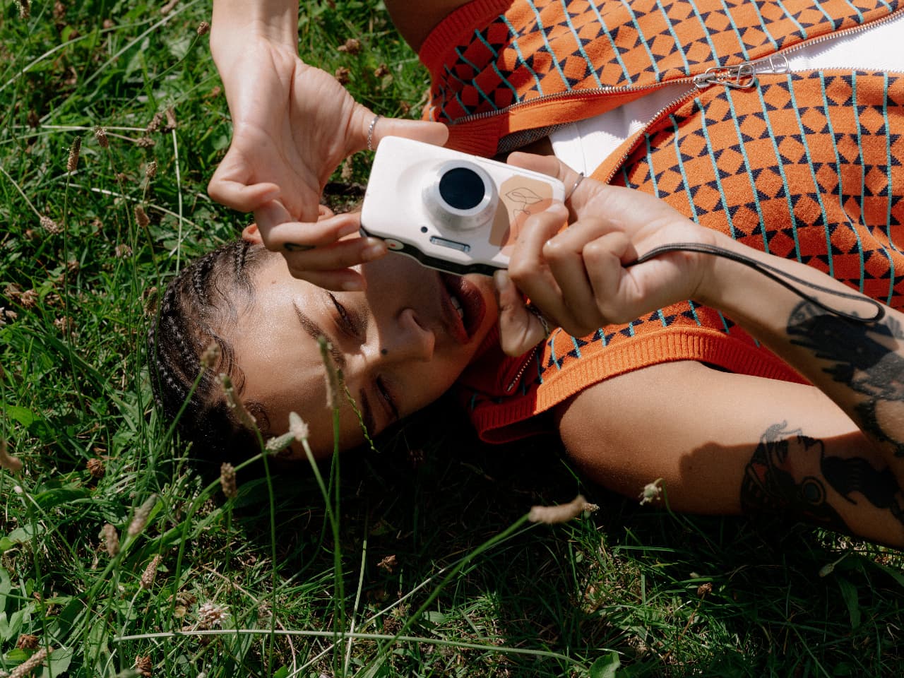 Person lying in the grass and taking a photograph with a compact camera